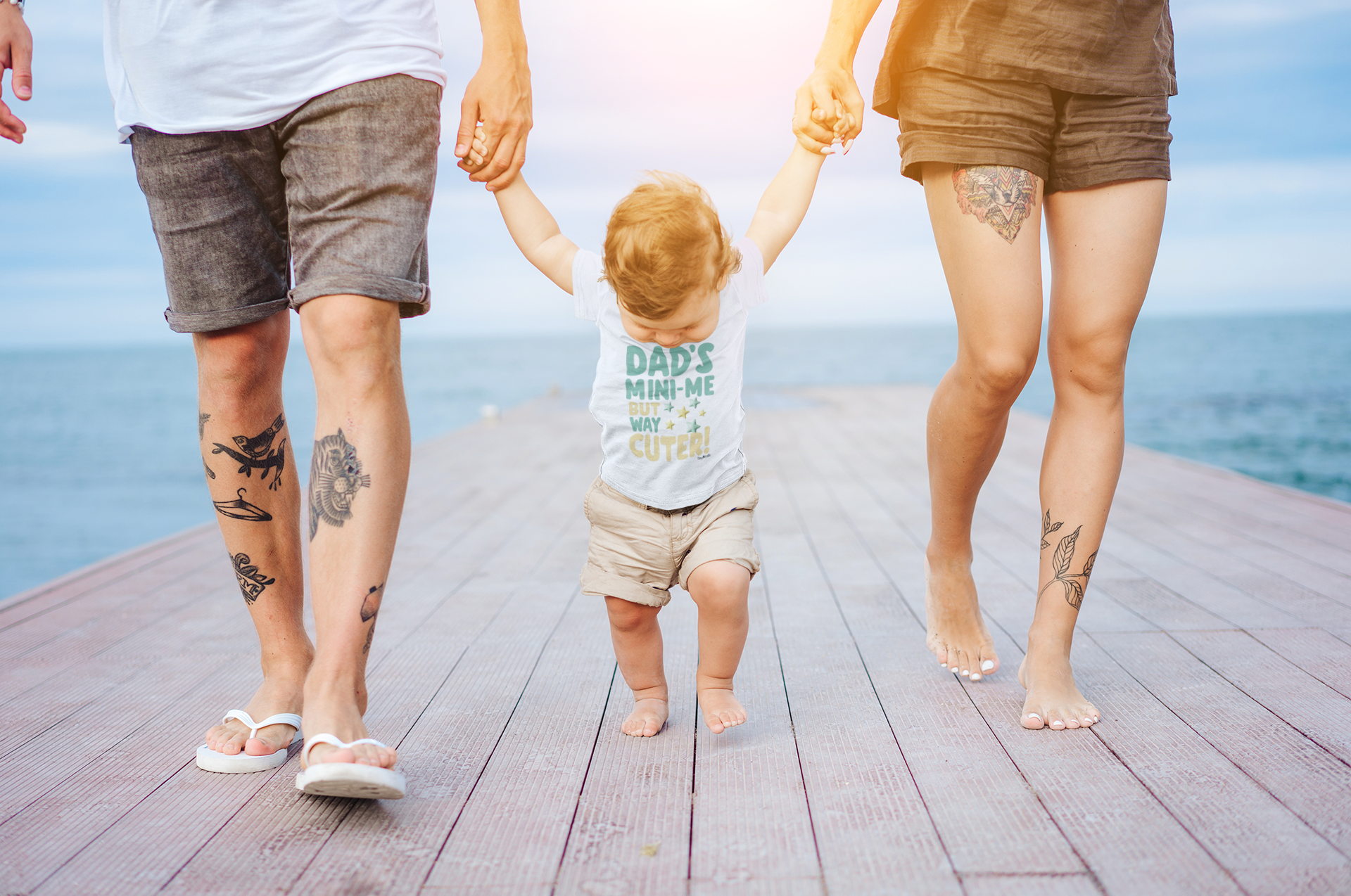 baby wearing a Dad's Mini Me But Way Cuter design on Crewneck T-shirt and holding mom and dad hand.